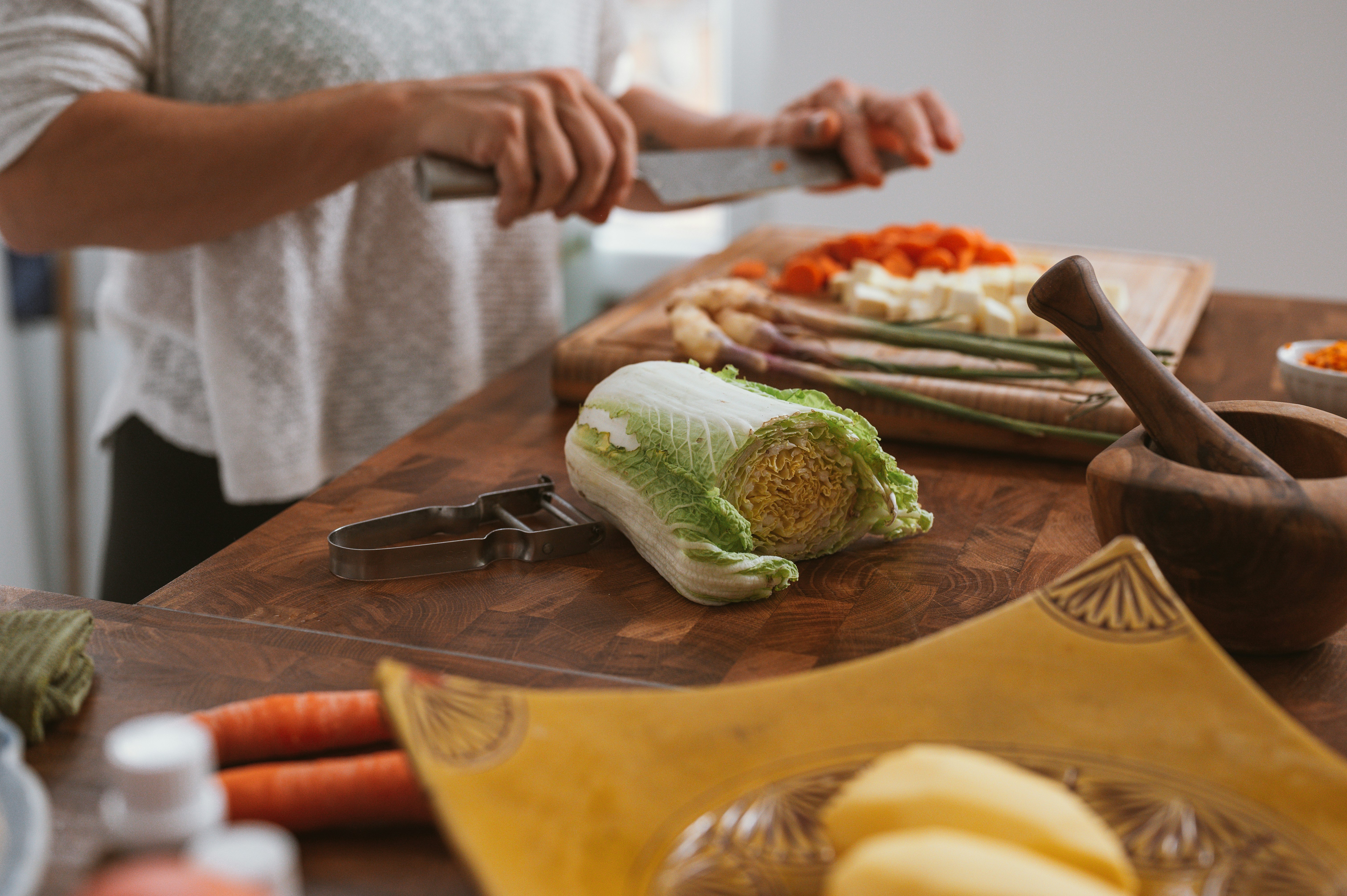 person slicing green vegetable on brown wooden chopping board